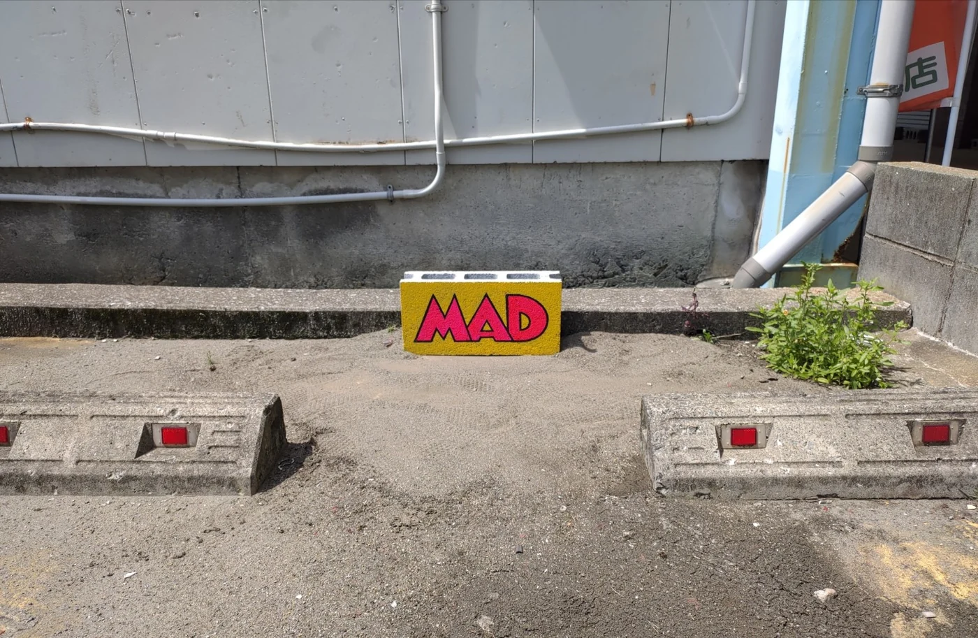 駐車場にある、黄色地に赤いMADの文字が描かれたブロック